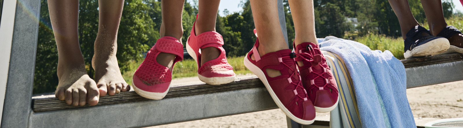 Barn i färgglada Reima-skor sitter på bänk vid stranden.