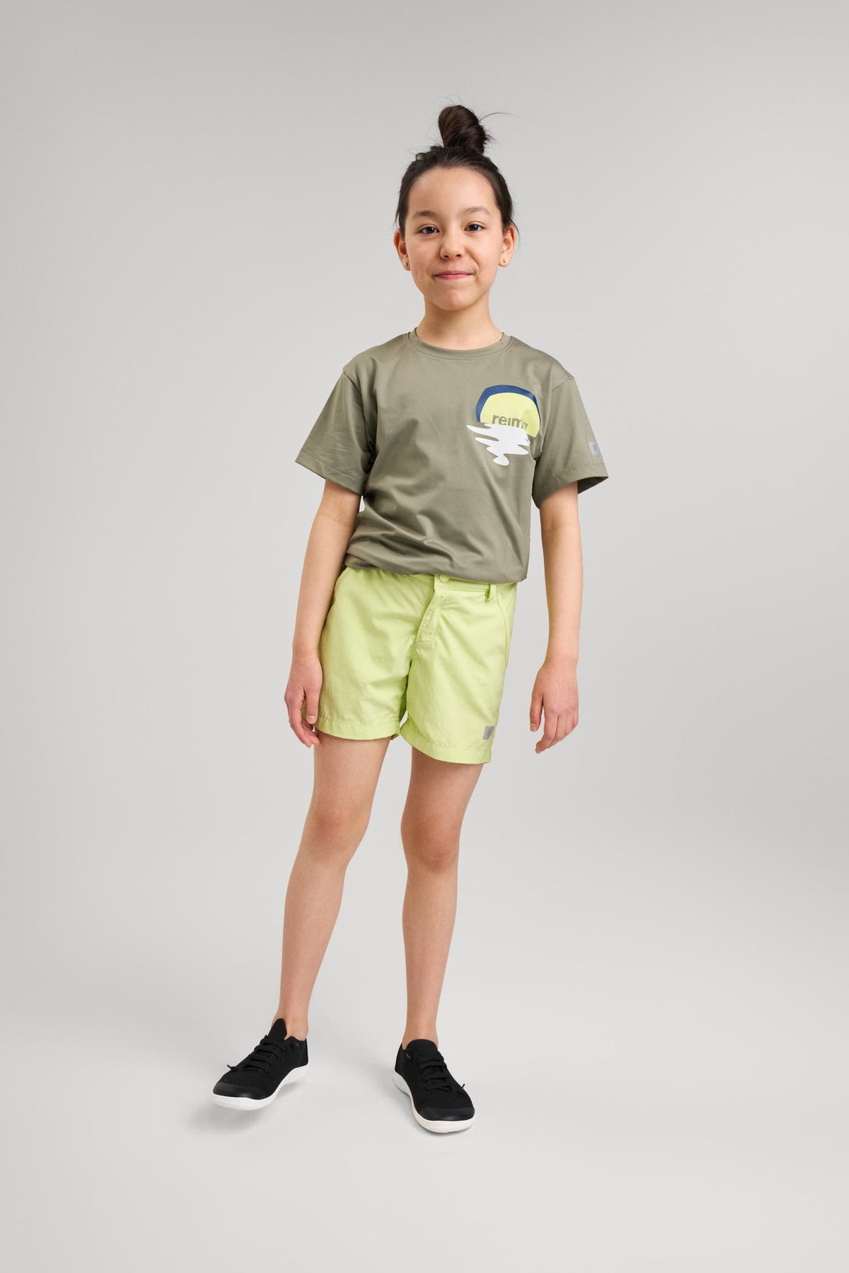 Reima barfotasko Astelu Black – svart minimalistisk sneaker för barn med vit sula, bärs här med ljusgröna shorts och grön t-shirt.