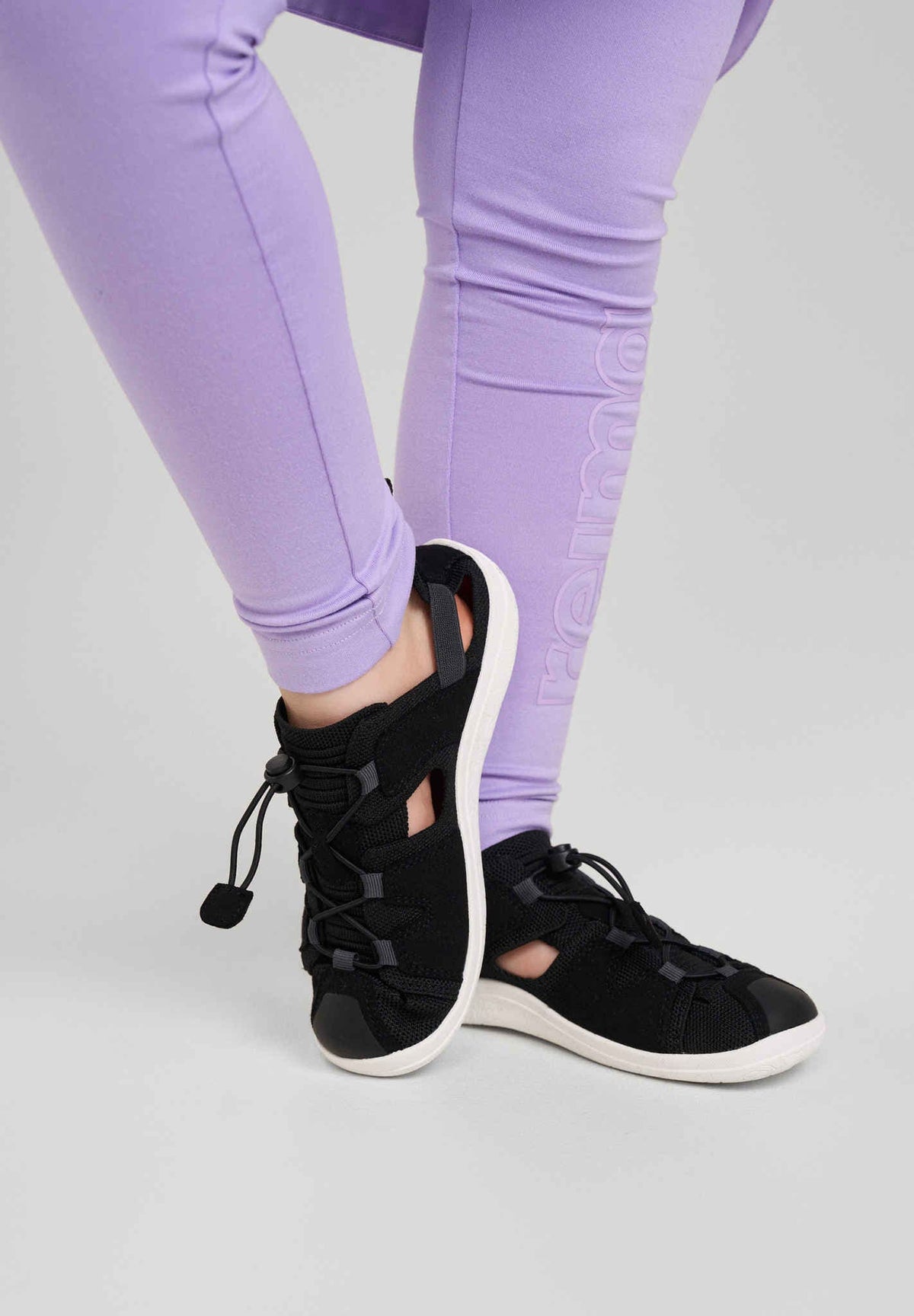 Reima barfotasko Black i användning – svart luftig barnsandal med vit sula och snabbsnörning, här buren tillsammans med lila leggings