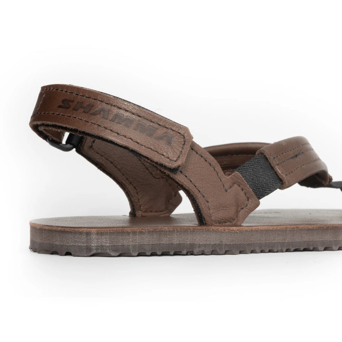 Närbild från sidan på Shamma Sandals Pacific Avenue i brunt läder, med justerbar hälrem och tydlig logotypprägling. Visar sandalens anatomiska passform, vadderade remmar och slitstarka sula för barfotakänsla vid promenader eller vandring.