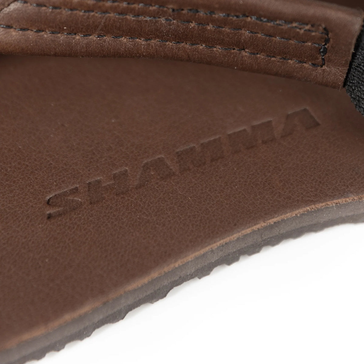 Närbild på fotbädden av Shamma Sandals Pacific Avenue i brunt läder, med präglad logotypen “SHAMMA” synlig i materialet. Bilden visar skons hantverkskvalitet och naturtrogna finish, vilket betonar sandalerna som barfotaskor med minimalistisk design.
