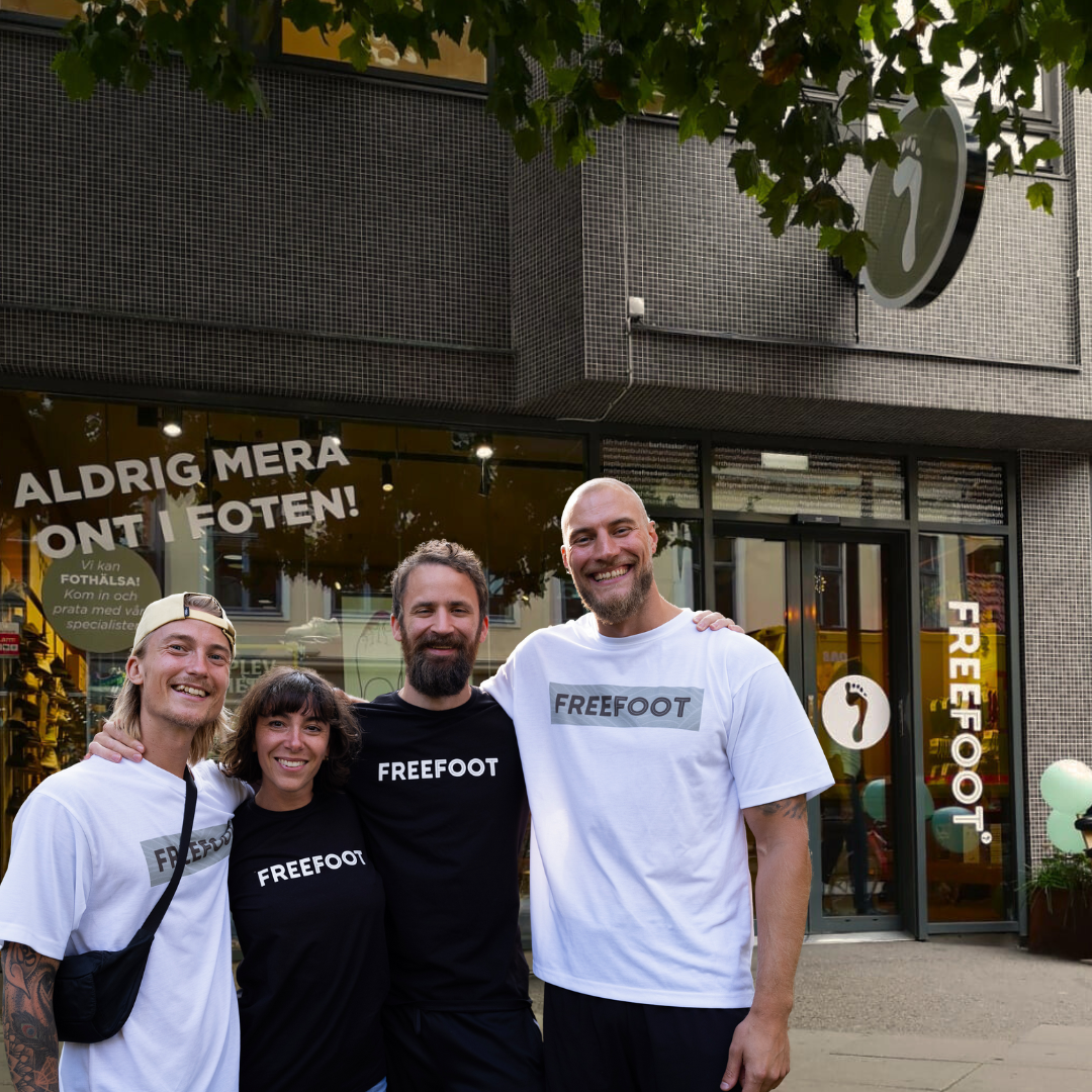Fyra medarbetare från Freefoot står leende framför butikens entré med skylten 'Aldrig mera ont i foten!' i bakgrunden. De bär Freefoot‑tröjor och visar en välkomnande atmosfär.