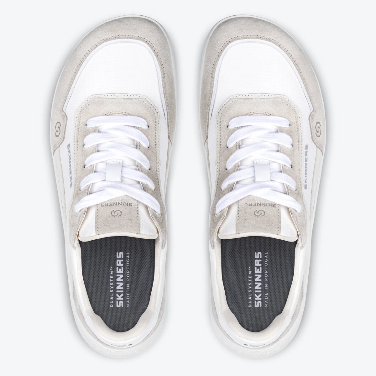 Produktbild av barfotaskon Skinners Allrounder White fotograferad uppifrån. Bilden visar ett par skor med bred tåbox, vit mesh och ljusgrå mockadetaljer. Skorna är parallellt placerade med tydlig sikt på snörning och innersula där Skinners-loggan och texten “Made in Portugal” är tryckta. Den symmetriska layouten framhäver skons minimalistiska och fotformade design.