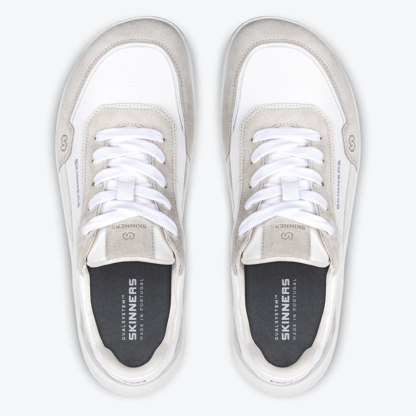 Produktbild på barfotaskon Skinners Allrounder White sedd från sidan. Skon har en låg, minimalistisk silhuett med vit sula, vit mesh och ljusgrå mockadetaljer. Skinners-loggan syns tydligt på sidan. Bilden är tagen mot ljus bakgrund med skon i profil, vilket visar dess breda tåbox och anatomiska form.