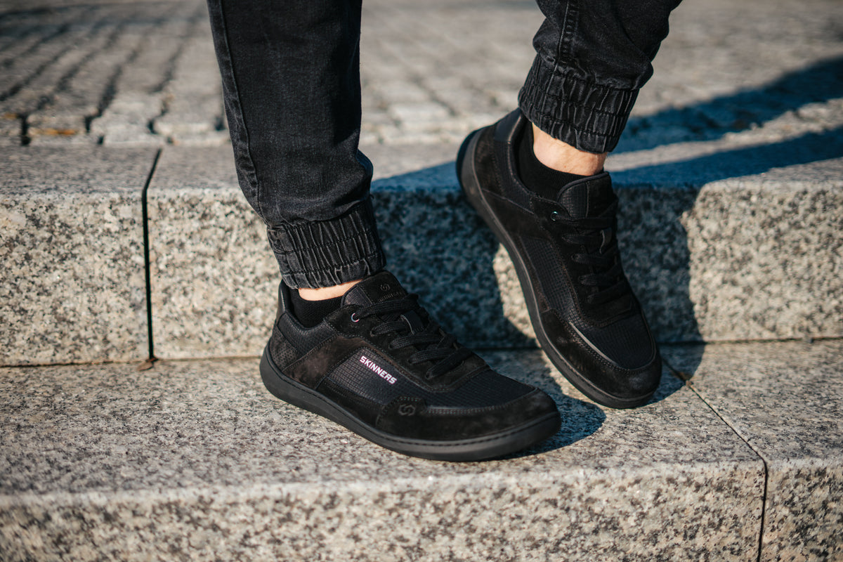 Person i svarta jeans står på trappsteg i ett par svarta Skinners Allrounder-skor
