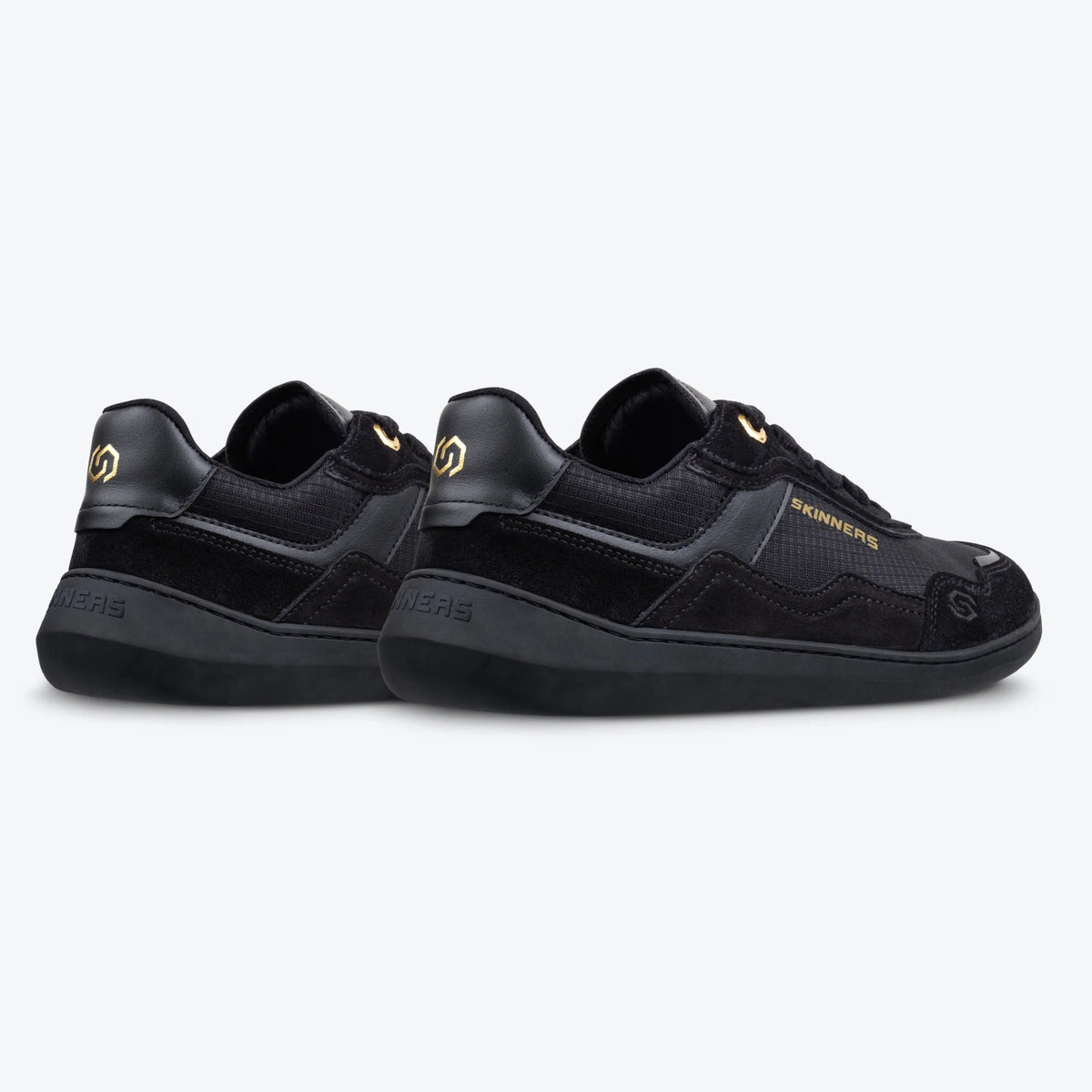 Produktbild på barfotaskor Skinners Camina Black – minimalistiska svarta sneakers i låg modell med bred tåbox, gulddetaljer och flexibel sula. Skorna visas från sidan och bakifrån i par.