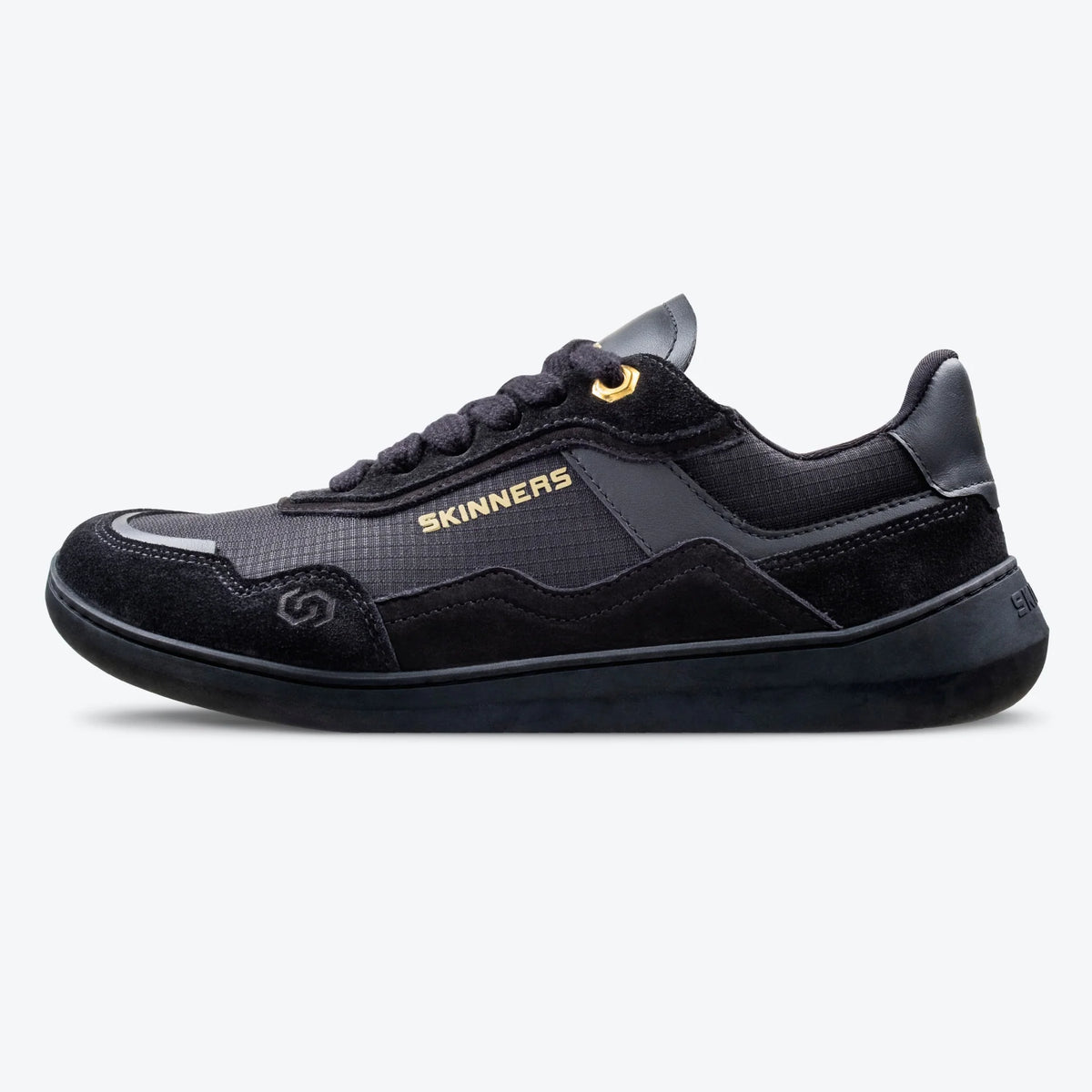Sidovy av barfotasko Skinners Camina Black – svart minimalistisk sneaker med bred tåbox, gulddetalj vid snörning och flexibel sula. Perfekt för naturlig fotrörelse och vardagsbruk.