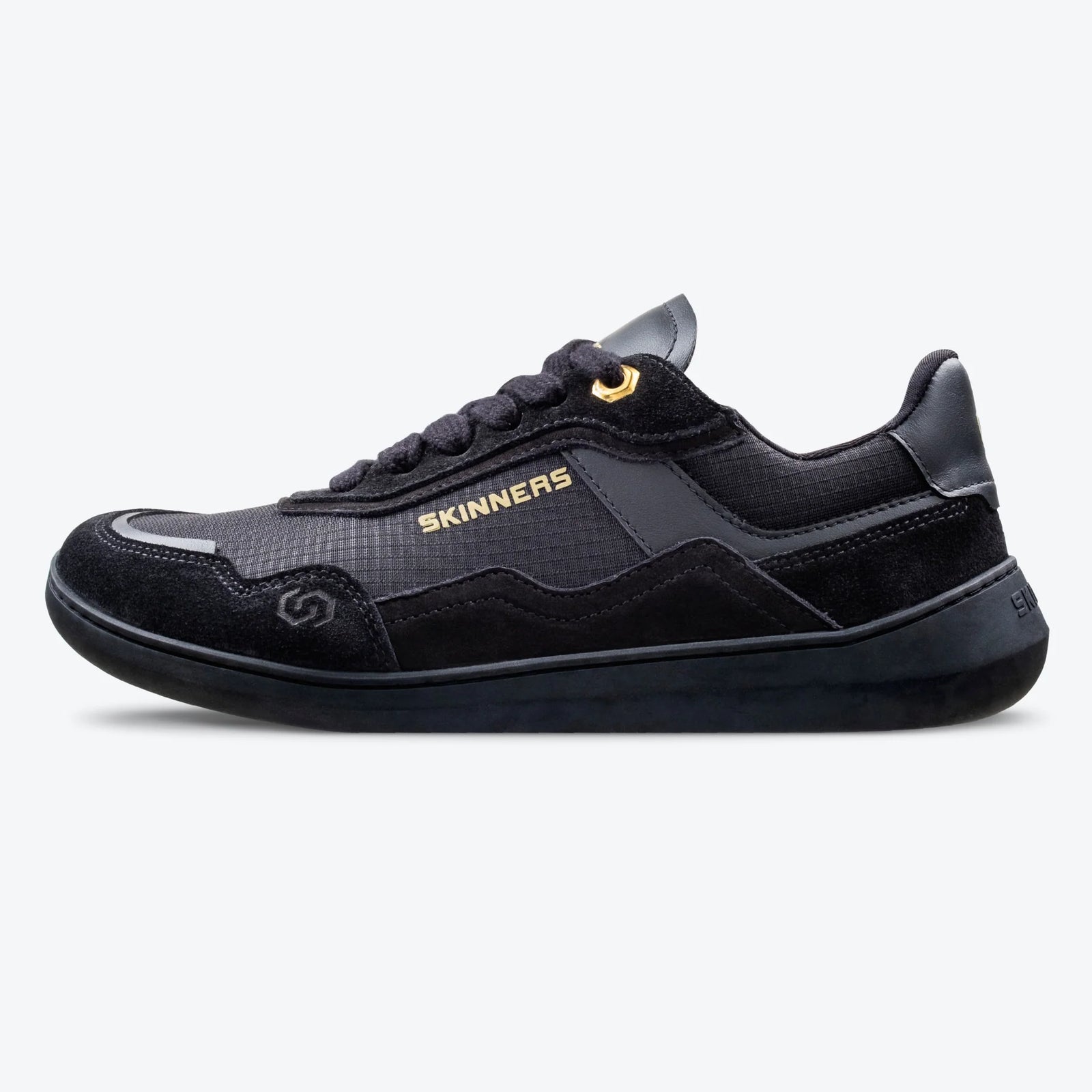 Sidovy av barfotasko Skinners Camina Black – svart minimalistisk sneaker med bred tåbox, gulddetalj vid snörning och flexibel sula. Perfekt för naturlig fotrörelse och vardagsbruk.