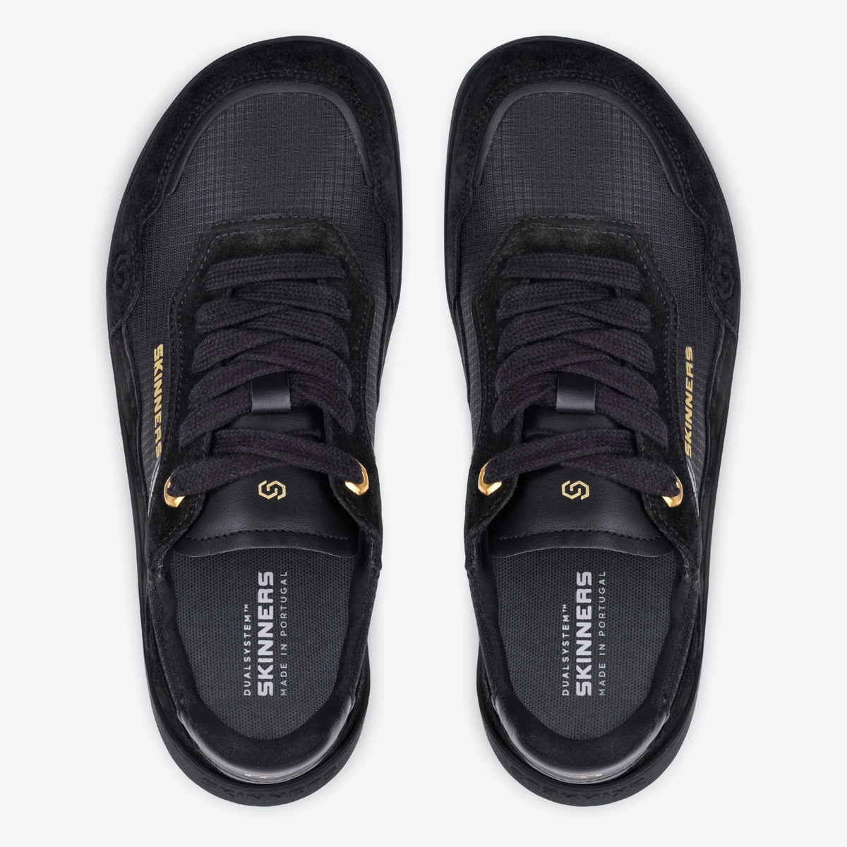 Topdown-vy av barfotaskor Skinners Camina Black – svarta sneakers med gulddetaljer och bred tåbox, designade för naturlig rörelse och optimal komfort. Märkt "Made in Portugal" och "DualSystem™".