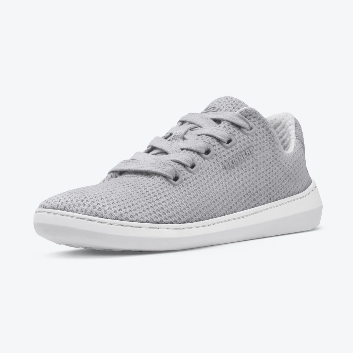 Produktbild på Skinners Globetrotter barfotaskor i färgen Cloudy Gray, visad snett framifrån. Skon har ett luftigt stickat mesh-övermaterial, diskreta grå skosnören och en vit minimalistisk barfotasula för naturlig rörelse